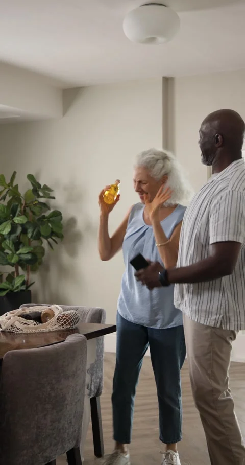 Vertical video: Unpacking bag sparking diverse senior couple dancing with olive Stock Footage 345320166