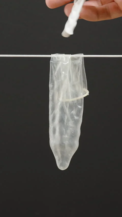 Vertical video. A used and washed condom is hanging on a clothesline with a Stock Footage 301172947