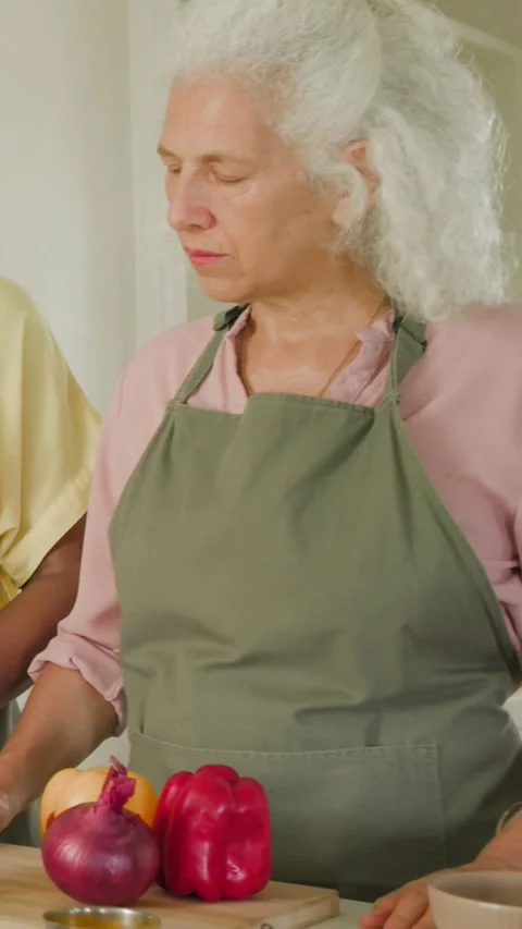 Vertical video: Using tablet recipe, two women in aprons chopping pepper at Stock Footage 348490940