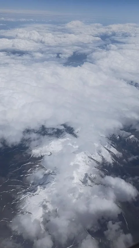 Vertical video of a view from a plane window, showing mountains and clouds below Stock Footage 308929393