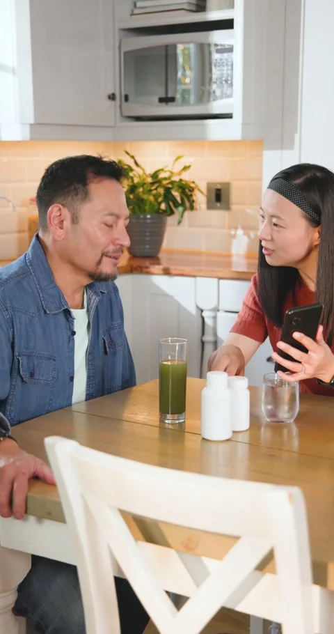 Vertical video: Viewing smartphone, Asian couple taking capsules with juice, Stock Footage 345491107