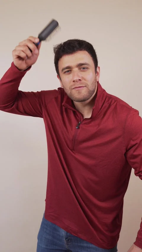 Vertical video of a white man, wearing an orange sweatshirt, combing his ha.. Stock Footage 236678048