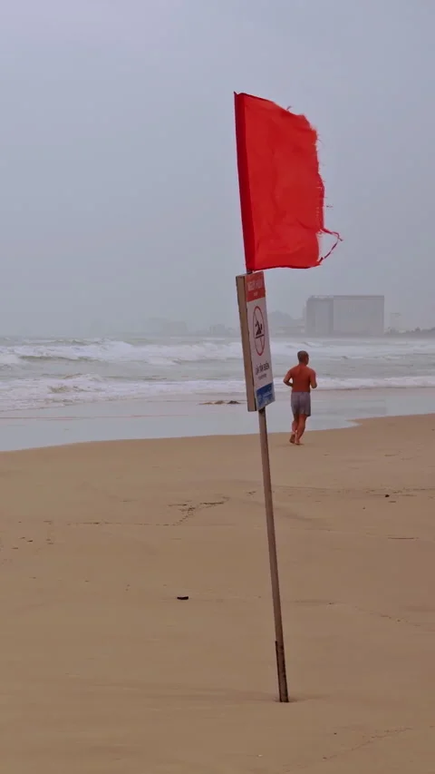 Vertical video. Wide Angle Slow Motion View of Red Warning Flag beside Strong Ch Stock Footage 323673835