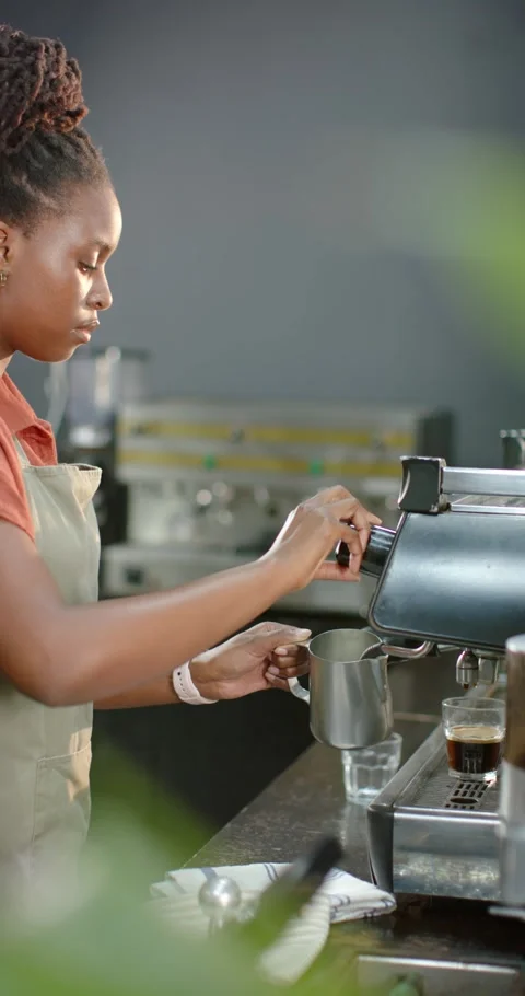 Vertical video: Woman in apron using steam knob and frothing milk pitcher for Stock-Footage 345218161