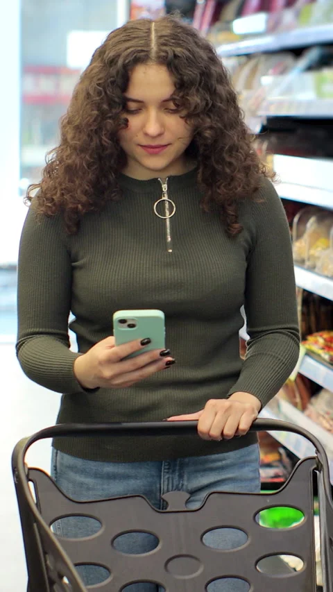 Vertical video. Woman checking list on smartphone while shopping. Stock Footage 346682327
