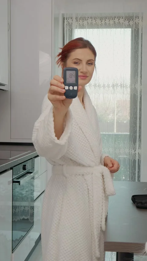 Vertical video Woman checks glucometer reading in kitchen for good diabetes Stock Footage 346714364