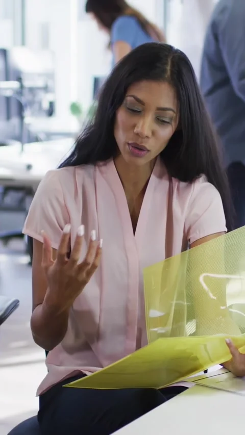 Vertical video: Woman explaining report to team flipping yellow folder HUD Stock Footage 334381958