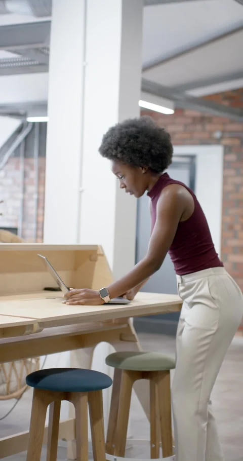 Vertical video: Woman in maroon checking watch walking to table starting work on Stock Footage 342036052