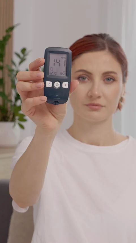 Vertical video Woman shows glucometer with high blood sugar reading of 141 mg dL Stock Footage 346714089