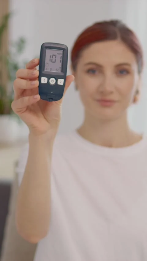 Vertical video Woman shows glucometer reading of 101 mg dL in home setting Stock Footage 346714102