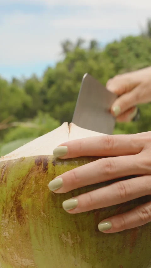 Vertical video. Woman Using Large Knife to Cut into Green Coconut Placed on Stock Footage 316167810