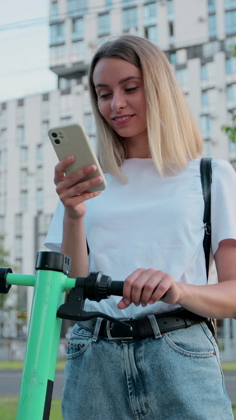 Vertical video. Woman using smartphone after ride on electric scooter Видео 344431012