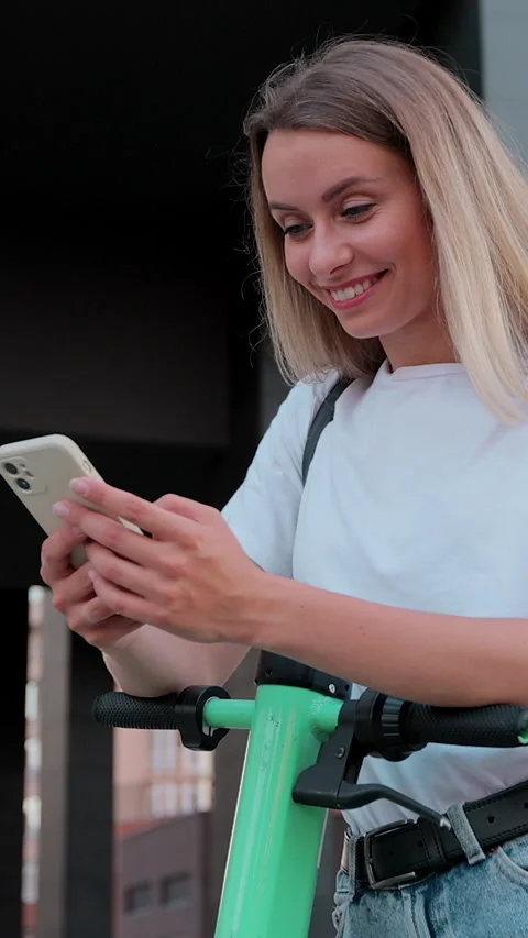 Vertical video. Woman is using smartphone after ride on electric kick scooter. Видео 344431805