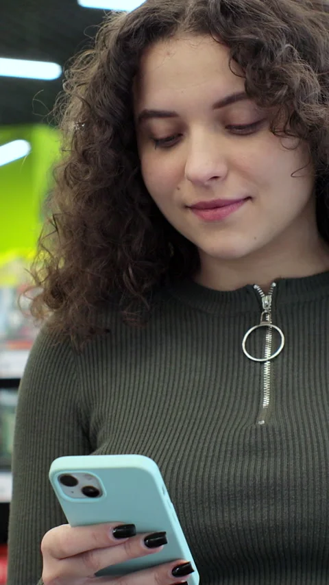 Vertical video. Woman using smartphone in supermarket with shopping trolley. Stock Footage 346682431