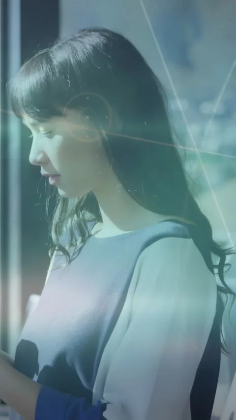 Vertical video: Woman by window tapping phone, demoing tech app as light rays Stock Footage 331166782