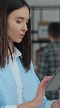 Vertical video. Worker checking inventory, writing notes on tablet. A woman w Stock Photos