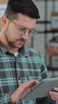 Vertical video. Worker checking inventory, writing notes on tablet. A man wor Stock Photos