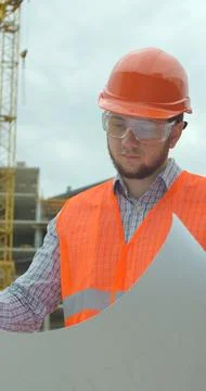 Vertical video. Young architect with hard hat holding blueprint in front of b Stock Photos