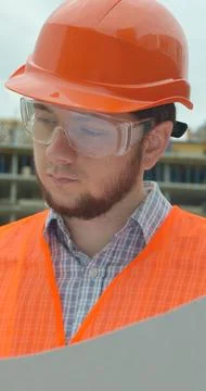 Vertical video. Young architect with hard hat holding blueprint in front of b Stock Photos