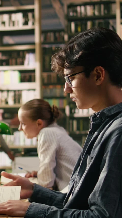 Vertical Video Young asian man with glasses reading book at library study table Stock Footage 336379427