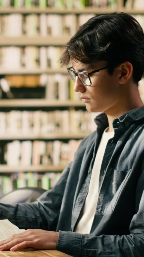 Vertical Video Young asian man with glasses reading book at library study table Stock Footage 336380529