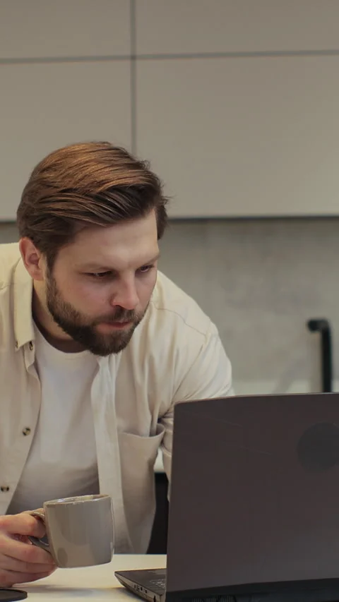 Vertical video. Young bearded man in his home in kitchen using laptop. Male Stock Footage 347779462