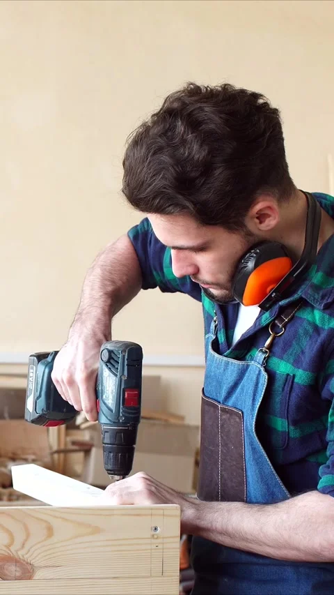 Vertical video of young carpenter in working apron assembles wooden structure Stock Footage 322972539