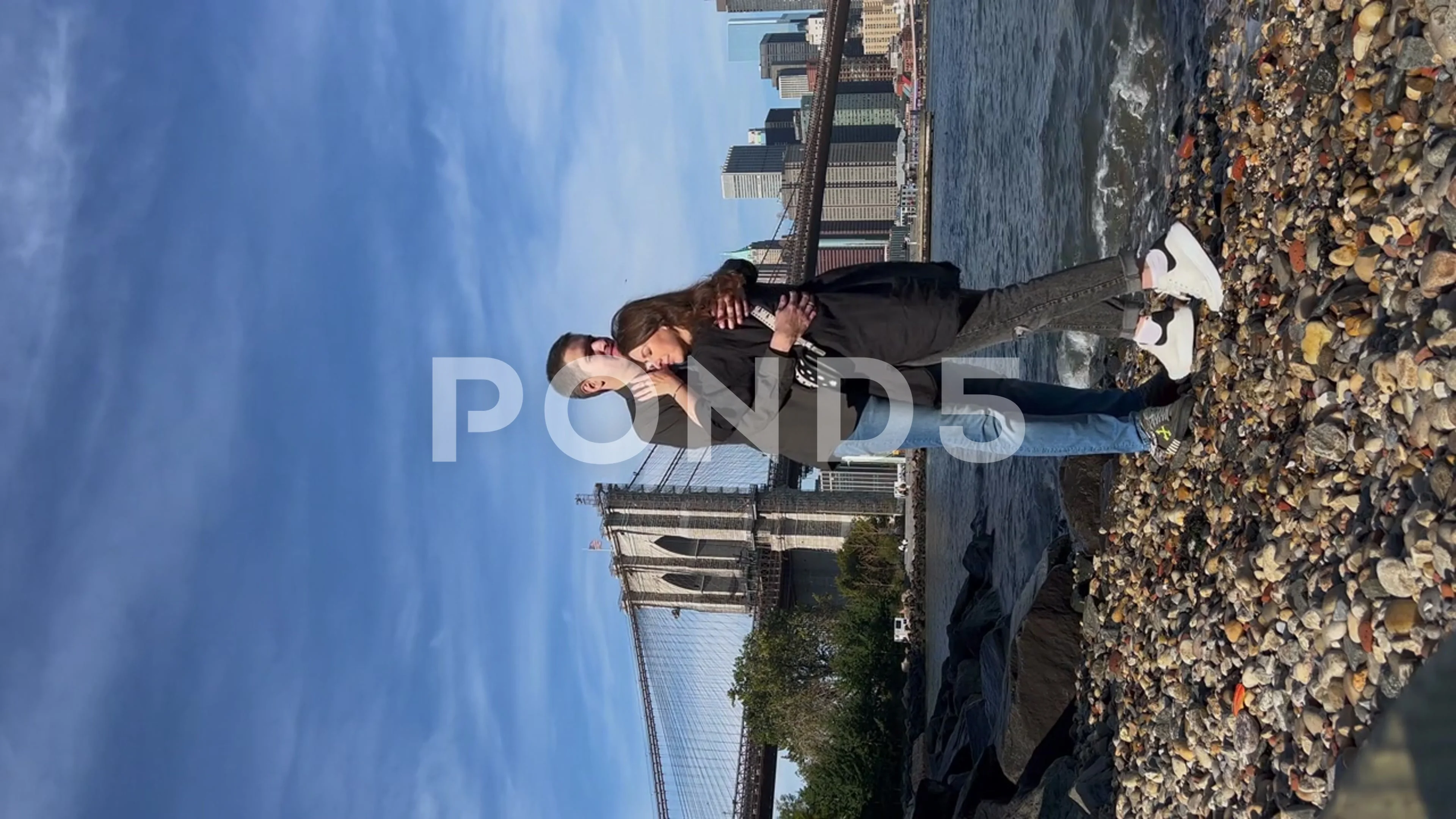 Vertical video. A young couple in love near the water with the Brooklyn  Bridge.