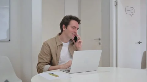 Vertical Video, Young Creative Man Talking on Phone While Working on Laptop Stock Footage 312914023