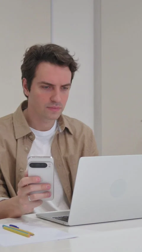 Vertical Video, Young Creative Man Using Phone and Typing on Laptop Stock Footage 318045012