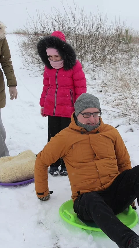Vertical video. A young dad in glasses gets on a sled and tries to push off with Stock Footage 301553992