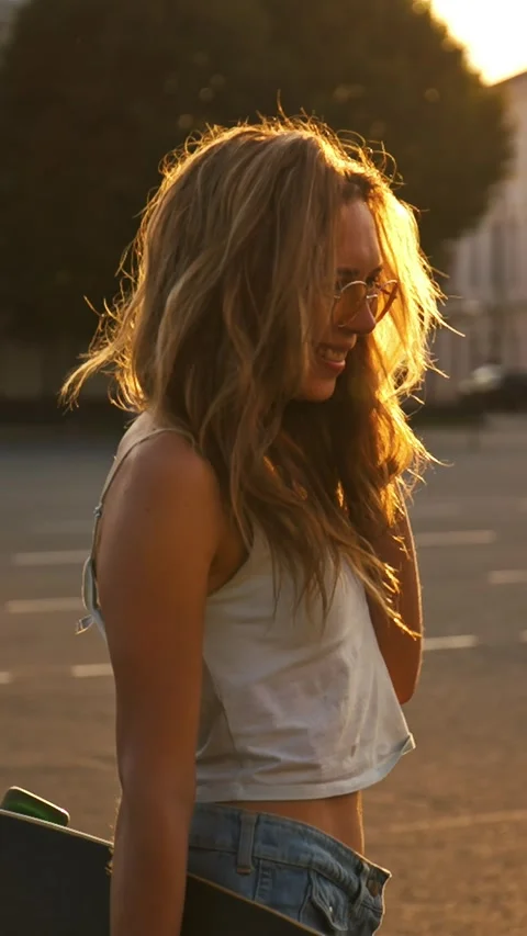 Vertical Video: Young happy smiling girl with skateboard at sunset on street Stock Footage 298947956