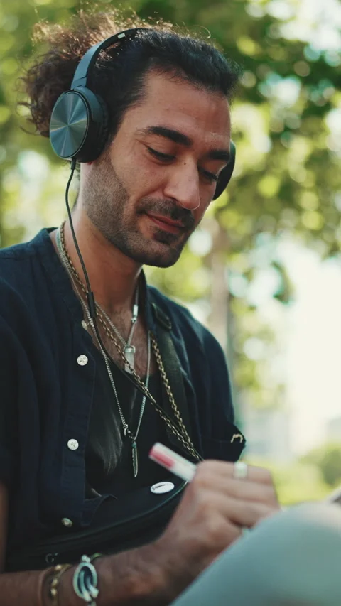 VERTICAL VIDEO: Young italian guy with ponytail and stubble sits on street bench 스톡 동영상 226951497