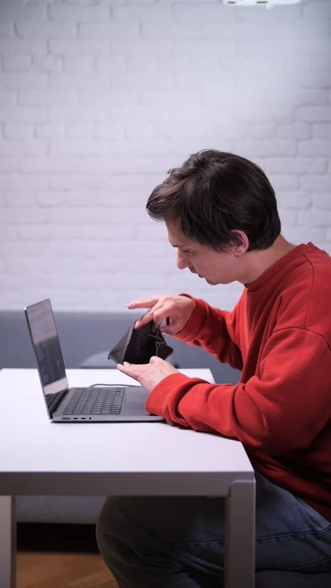 Vertical video Young man checking empty wallet while working at home on laptop Stock Footage 311202393