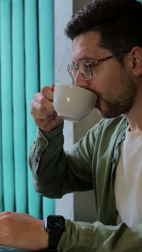 Vertical video. Young man with coffee multitasking on laptop. Video stock 345236751
