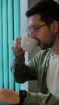 Vertical video. Young man with coffee multitasking on laptop. Stock Photos