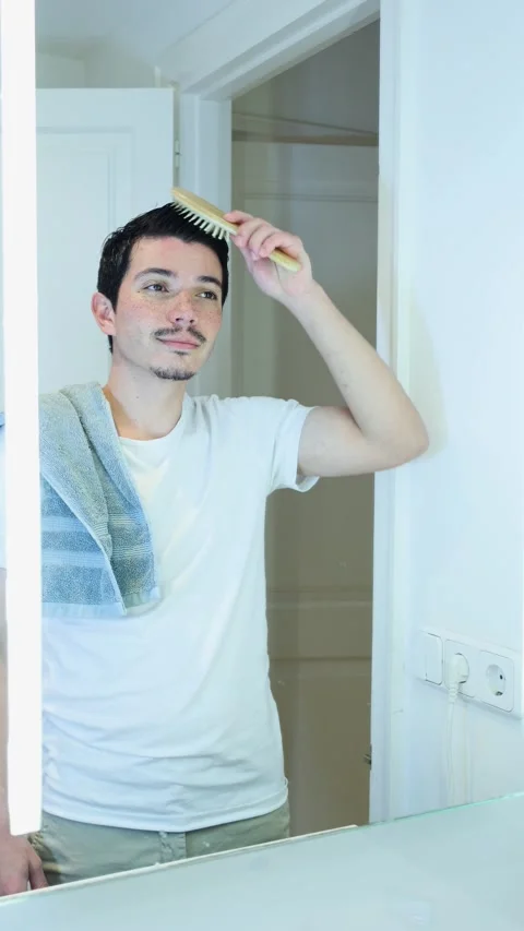 Vertical video of young man combing his hair with a wooden comb after takin.. Stock Footage 297666110
