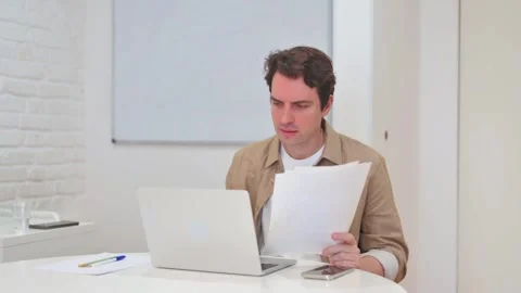 Vertical Video, Young Man Cursing Paperwork Results while Working on Laptop Stock Footage 312914383