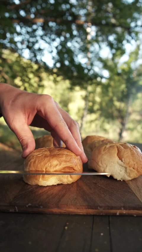 Vertical video of young man cutting burger buns on wooden board outdoors Stock Footage 286310091