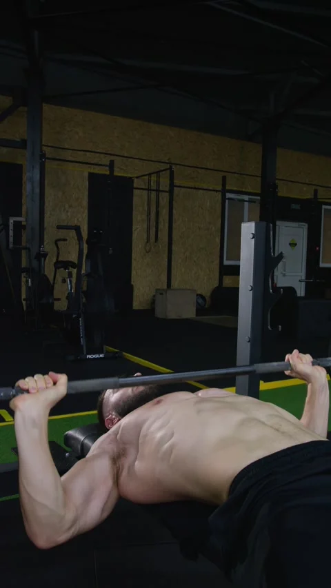 Vertical video. A young man does exercises with a barbell in a dark hall. Video stock 281868548