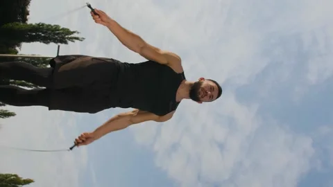 Vertical video. A young man jumps on a skipping rope outdoors in front Stock Footage 220131854