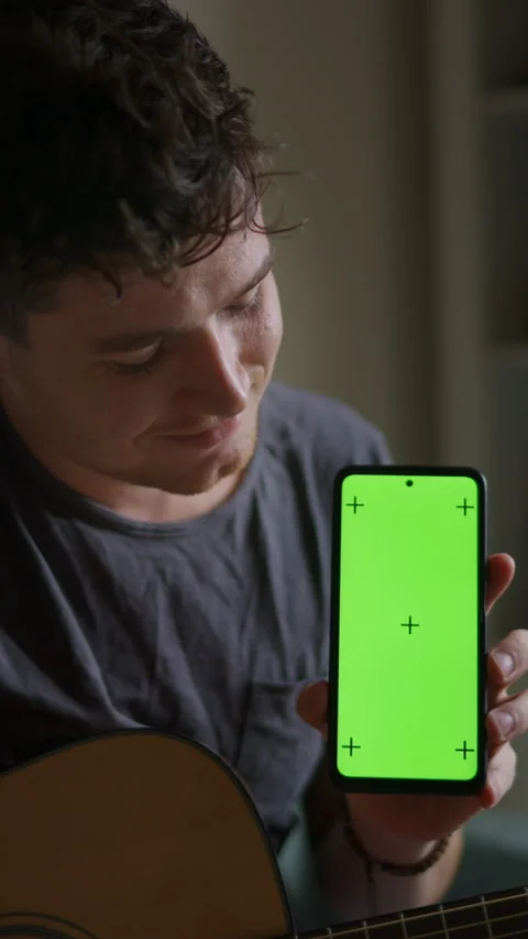 Vertical video: Young man plays guitar learns from smartphone app. Smartphone Stock Footage 298729660
