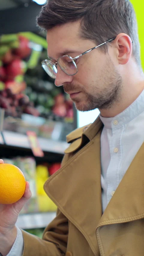 Vertical video. Young man selecting fresh oranges in a supermarket. Stock Footage 346684039