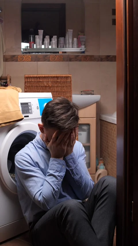 Vertical video young man sitting on the bathroom floor, covering his face with Stock Footage 324761371