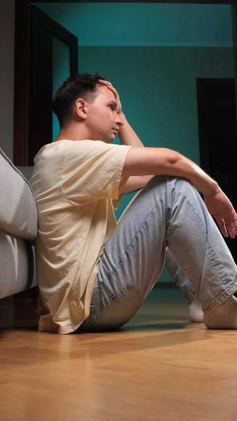 Vertical video young man sitting on the wooden floor at home, leaning against a Stock Footage 342771475