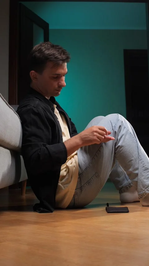 Vertical video young man sitting on the floor, holding an empty wallet over his Stock Footage 342772745