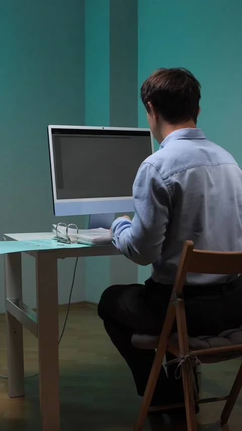 Vertical video young man sitting at a desk, focused on working with a computer Stock Footage 345532243