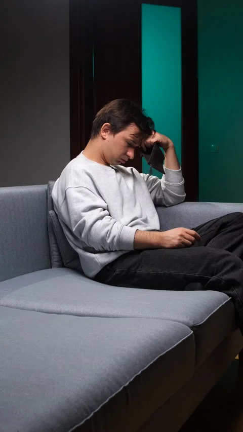 Vertical video young man sitting on sofa at home, holding an empty wallet and Stock Footage 346251005