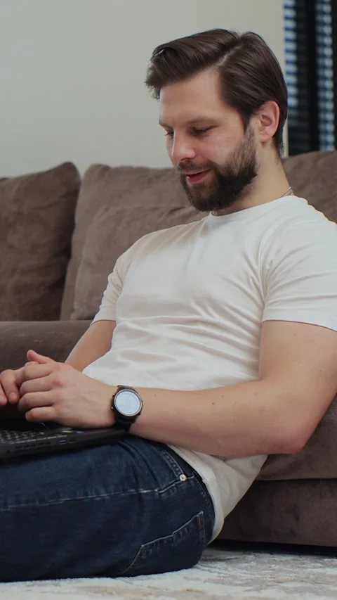 Vertical video. Young man sitting on the living floor room at home using laptop Stock Footage 347780035