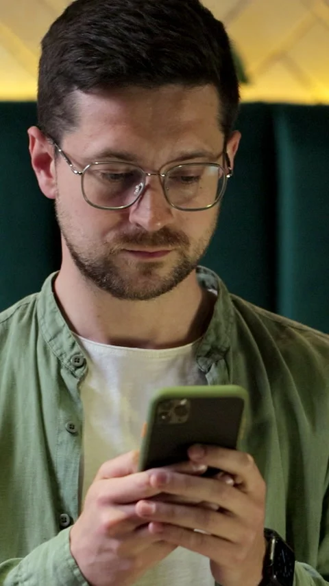 Vertical video. Young man using smartphone at cafe for messaging and browsing. Stock Footage 345238067